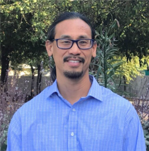 a person in a blue shirt and glasses standing in front of trees